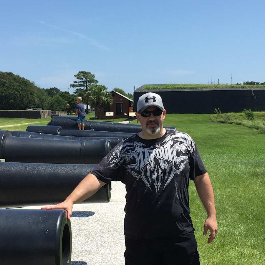 Sig. Alexander outdoors beside a row of old cannons, wearing a cap and sunglasses.